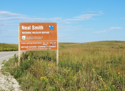 Sign for Neal Smith National Wildlife Refuge, with grassy landscape and blue sky in the background.