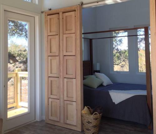 Cozy bedroom with a wooden sliding door, large windows, and a neatly made bed with gray bedding and a basket nearby.
