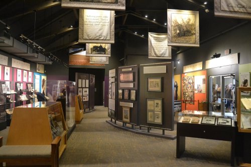 Interior of a museum exhibit featuring framed artworks, photographs, and informational panels displayed on walls.