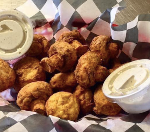 A basket of golden-brown fried shrimp with two dipping sauces on a checkered paper lining.