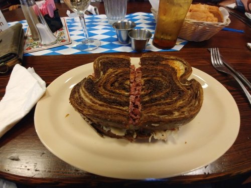 A sliced sandwich on a plate, featuring layers of dark rye bread and corned beef, served with small dipping sauces.