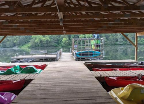 A wooden dock with colorful kayaks lined up, leading to a calm lake surrounded by greenery.