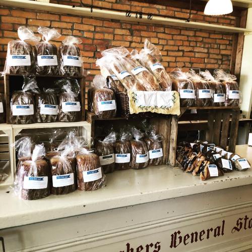 A display of various baked goods in clear bags, arranged on wooden shelves in a rustic shop setting.
