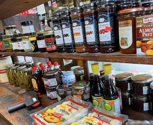 A wooden shelf filled with various jars of jams, sauces, and preserves, alongside snacks and condiments.