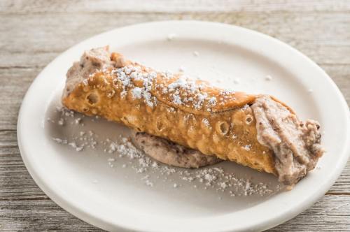 A crispy cannoli filled with creamy filling, dusted with powdered sugar, on a white plate.