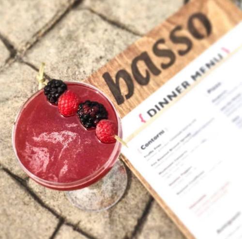 A vibrant cocktail garnished with raspberries and blackberries, next to a dinner menu on a textured surface.