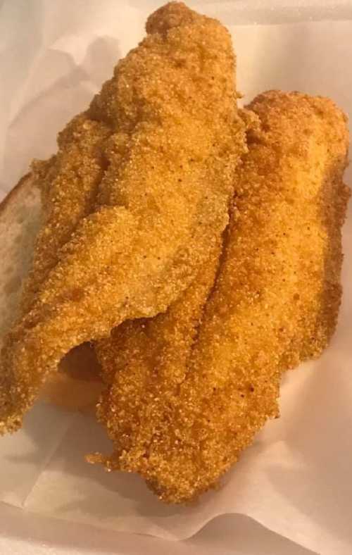 Two golden-brown fried fish fillets on a slice of bread, served on a white paper background.