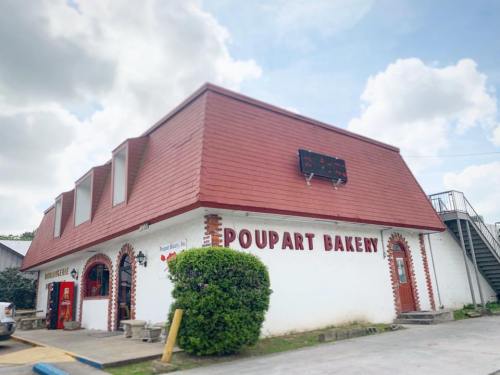 Exterior of Pourpart Bakery, featuring a red roof and white walls, with decorative arches and a green bush in front.