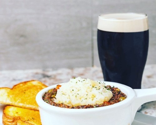 A bowl of shepherd's pie topped with mashed potatoes, served with toast and a pint of dark beer.