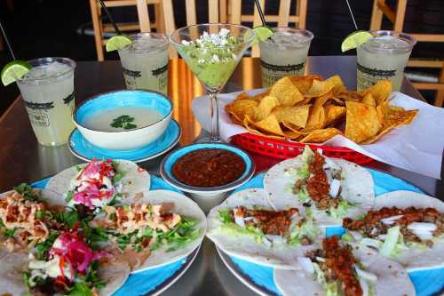 A vibrant spread of tacos, guacamole, chips, and drinks on a table, showcasing a delicious Mexican feast.