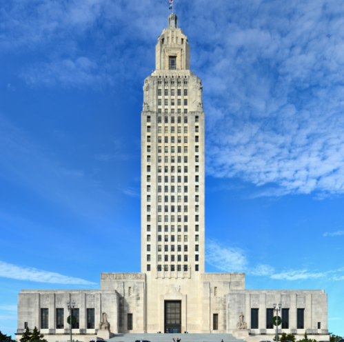 A tall, Art Deco-style building with a spire, set against a blue sky with scattered clouds.
