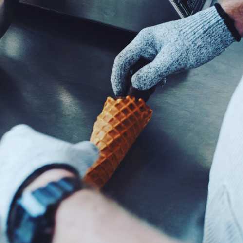 A person wearing gloves holds an ice cream cone, preparing to fill it with ice cream.