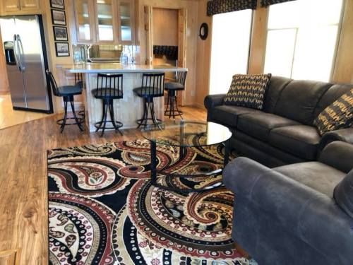 Cozy living area with a dark sofa, glass coffee table, patterned rug, and a kitchen bar with stools in the background.