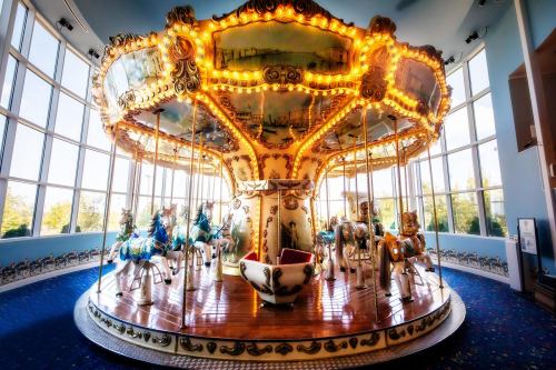 A brightly lit carousel with ornate horses, set in a spacious room with large windows.