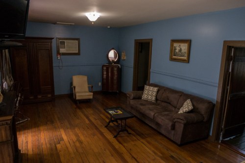 Cozy living room with a brown sofa, wooden floor, blue walls, and a small table, featuring a chair and decorative items.