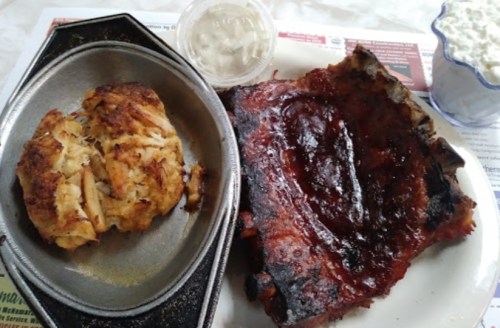 A plate featuring a crab cake and a portion of barbecue ribs with a side of dipping sauce.