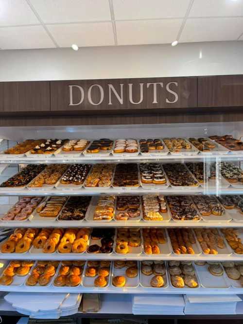 A display case filled with a variety of colorful donuts arranged on trays under a sign that reads "DONUTS."