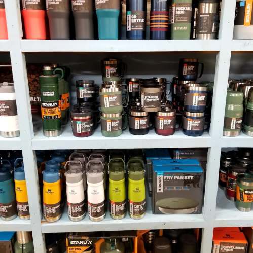 A display of various Stanley drinkware and cookware, including bottles, mugs, and a frying pan set on shelves.