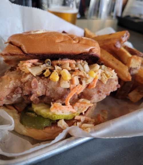 A crispy fried chicken sandwich topped with slaw and pickles, served with a side of golden French fries.