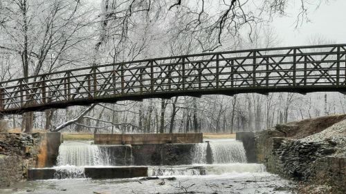 A wooden bridge spans a snowy landscape with a waterfall cascading over stone steps below.