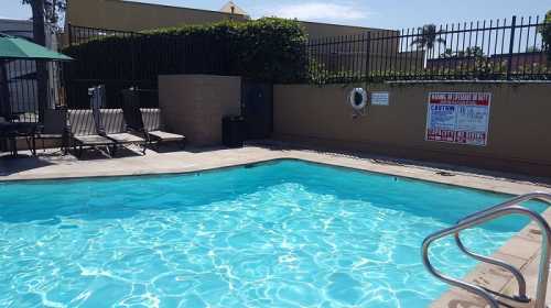 A clear blue swimming pool surrounded by lounge chairs and a fence, with a sign warning about pool safety.