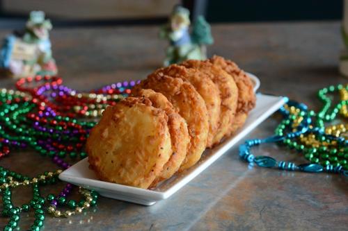 A platter of golden-brown fried cookies surrounded by colorful festive beads on a table.