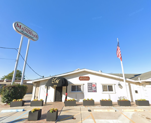 Exterior of Mandina's restaurant with a sign, American flag, and flower planters in front.