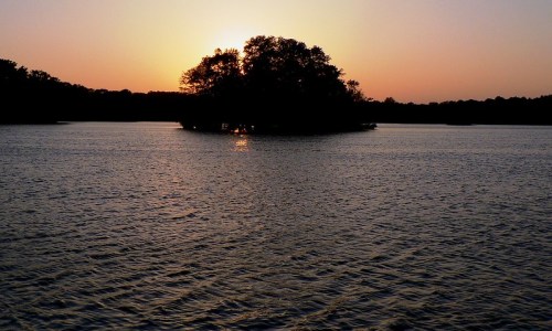 Sunset over a calm lake, with a small island silhouetted against the colorful sky.