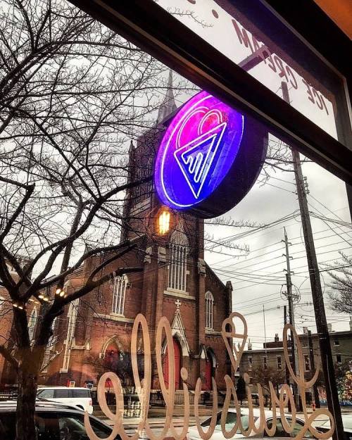 View from a window featuring a neon heart sign and a church in the background, with trees and power lines visible.