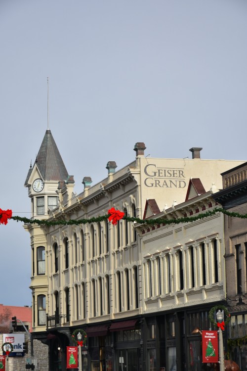 Historic buildings with a clock tower and "Geiser Grand" sign, decorated for the holidays.
