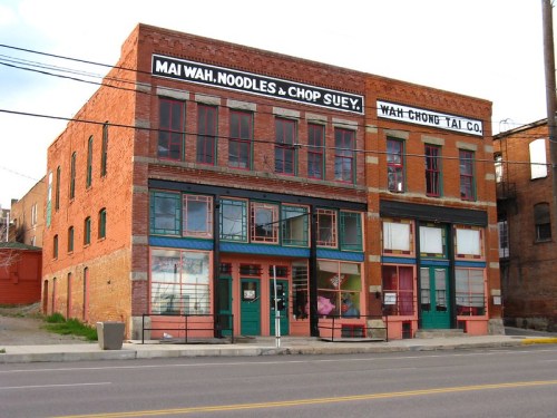 Historic brick building with colorful storefronts, featuring signs for "Mai Wah Noodles & Chop Suey" and "Wah Chong Tai Co."