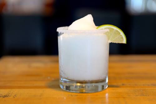 A frosty cocktail in a glass, garnished with a lime slice and served on a wooden table.