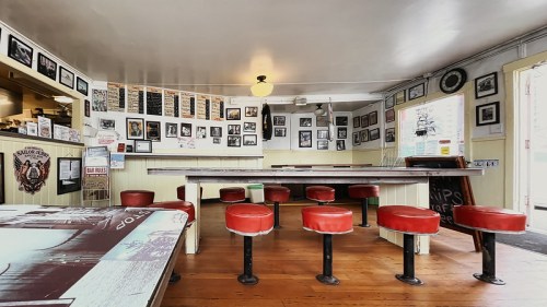 A cozy diner interior with red stools, wooden tables, and walls adorned with black-and-white photos and signs.