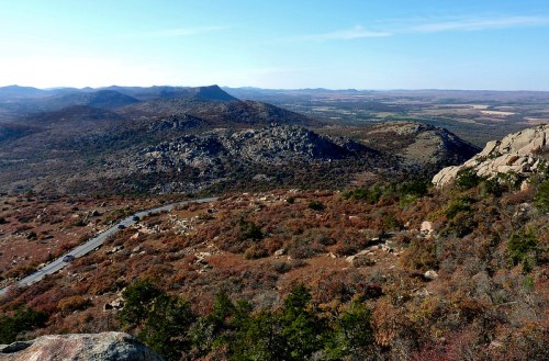 A panoramic view of rolling hills and rocky terrain under a clear blue sky, showcasing autumn foliage.