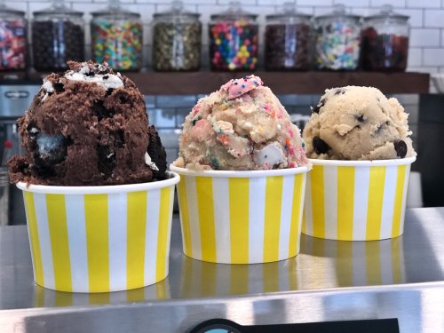 Three colorful ice cream scoops in yellow-striped cups, featuring chocolate, birthday cake, and cookie dough flavors.