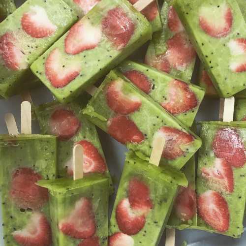 Colorful popsicles with green layers and pieces of strawberries, arranged with wooden sticks.