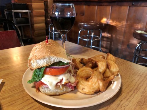 A plate with a sandwich topped with lettuce, tomato, and cheese, accompanied by curly fries and a glass of red wine.
