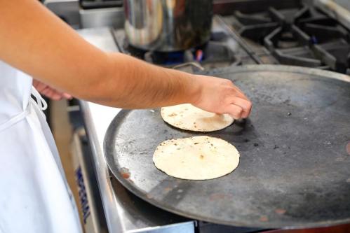 A hand places tortillas on a hot griddle in a kitchen setting.