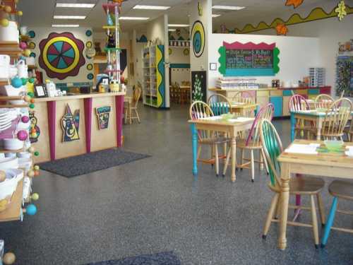 Brightly colored pottery studio with tables, chairs, and shelves filled with art supplies. Cozy and inviting atmosphere.