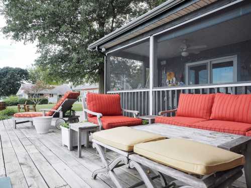 A cozy outdoor patio with red cushions, wooden furniture, and a screened-in area surrounded by greenery.