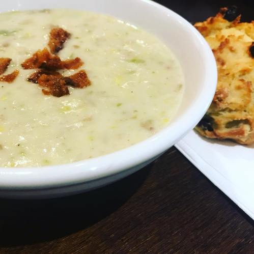 A bowl of creamy soup topped with crispy bits, served alongside a piece of bread on a napkin.