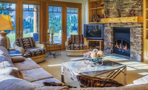 Cozy living room with stone fireplace, large windows, and comfortable seating, overlooking a scenic outdoor view.