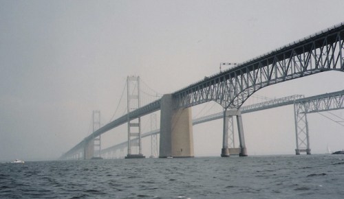 A foggy view of a large bridge spanning over water, with multiple arches and support structures visible.