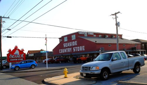 A red building labeled "Seaside Country Store" with a sign and parked cars on a sunny day.