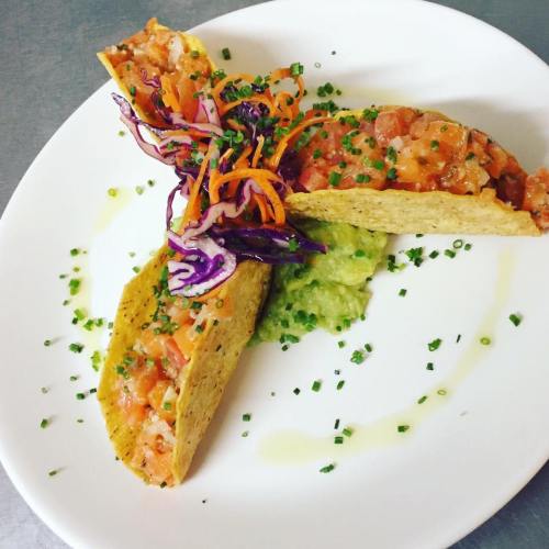 Two tacos filled with diced tomatoes and topped with colorful slaw, served on a white plate with guacamole.