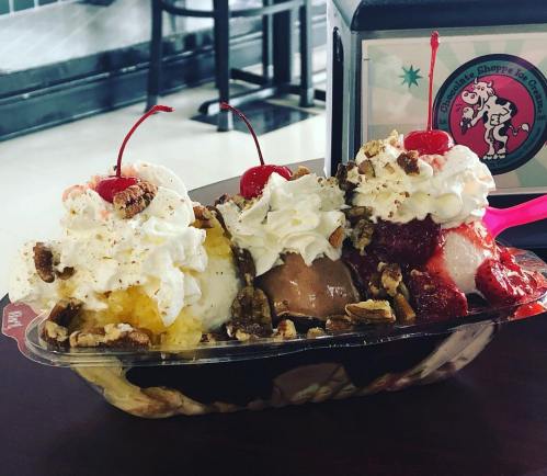 A colorful ice cream sundae with three scoops, whipped cream, nuts, and cherries on top, served in a boat dish.