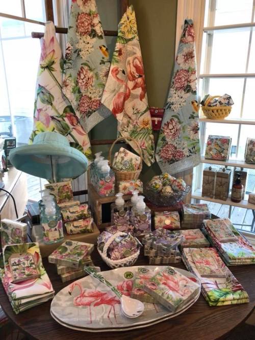 A colorful display of floral-themed kitchenware, towels, and soaps arranged on a wooden table.