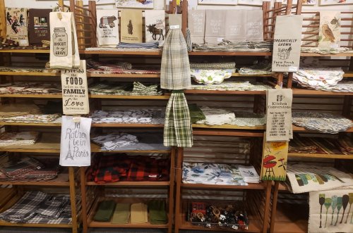 Shelves filled with various kitchen linens, including towels, tablecloths, and decorative items in different patterns.