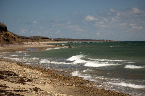 A serene beach scene with gentle waves, rocky shore, and a cloudy sky in the background.