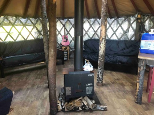 Interior of a yurt featuring a wood stove, seating area, and a guitar in the background.